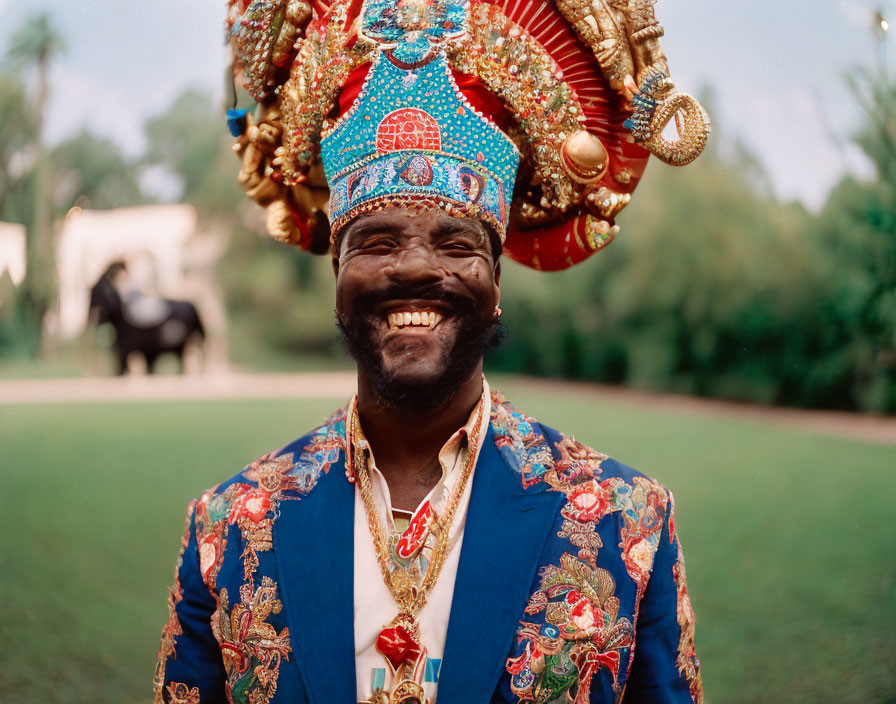 Joyful man in bejeweled crown and blue attire with elephant in background