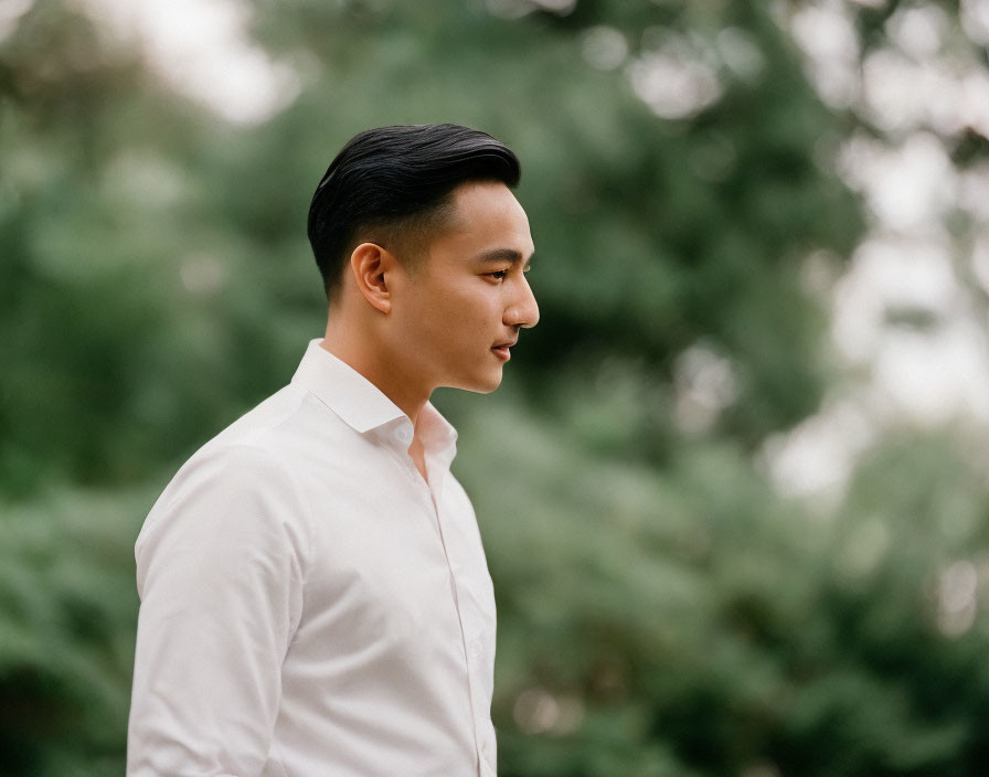 Young man in white shirt in outdoor setting with greenery.