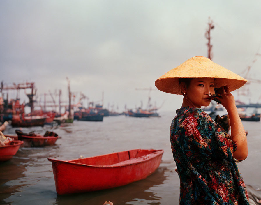 Person in straw hat by red boats with ships and hazy sky