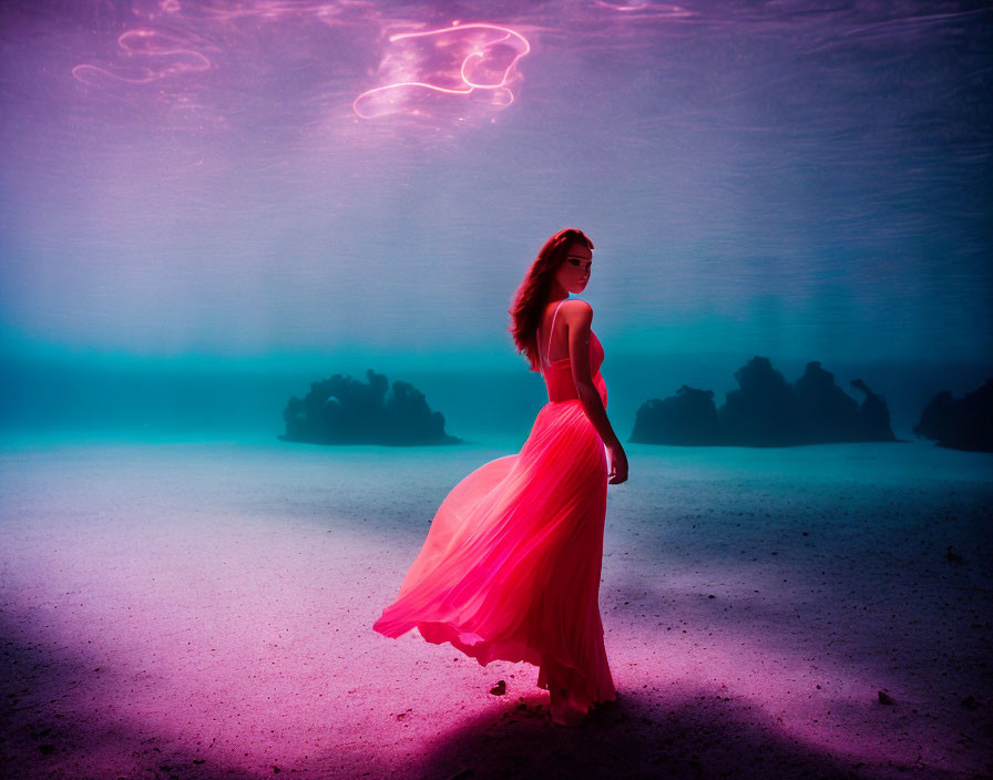 Woman in flowing red dress underwater with pink and blue lighting and rock formations