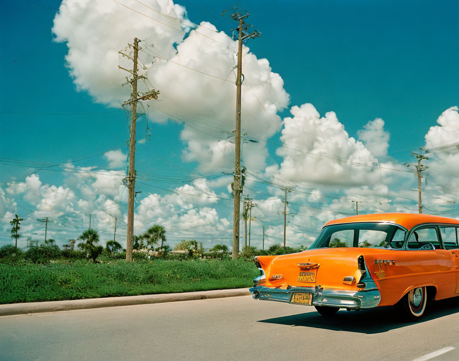 Vintage orange car parked on sunny road with white clouds and electricity poles