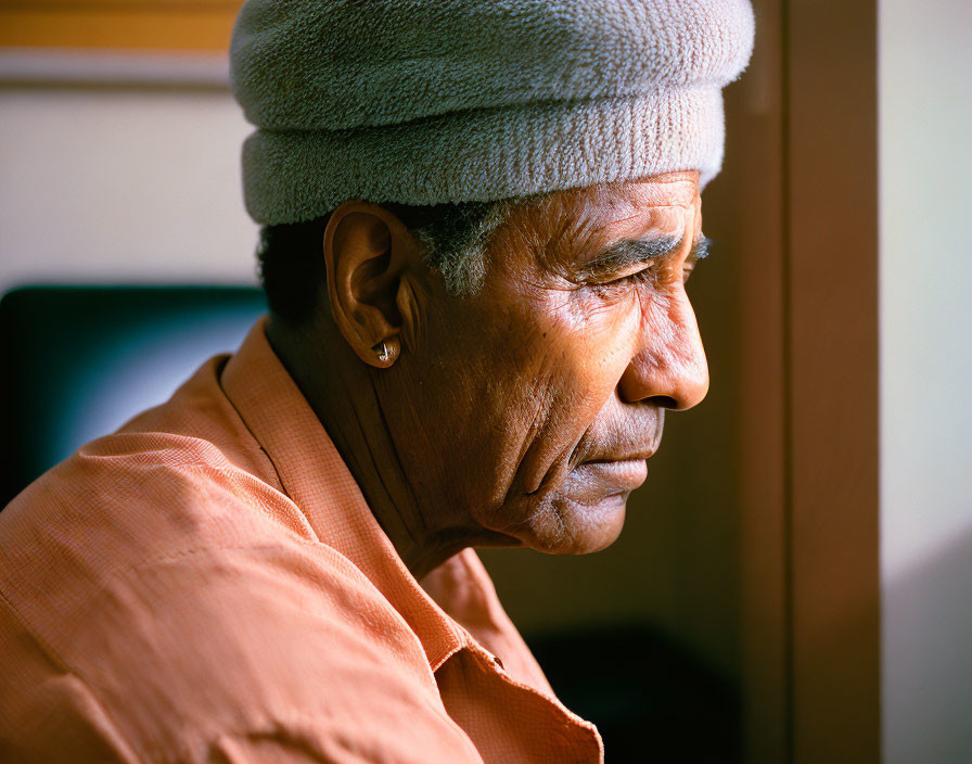 Elderly person with towel on head in orange shirt gazes sideways