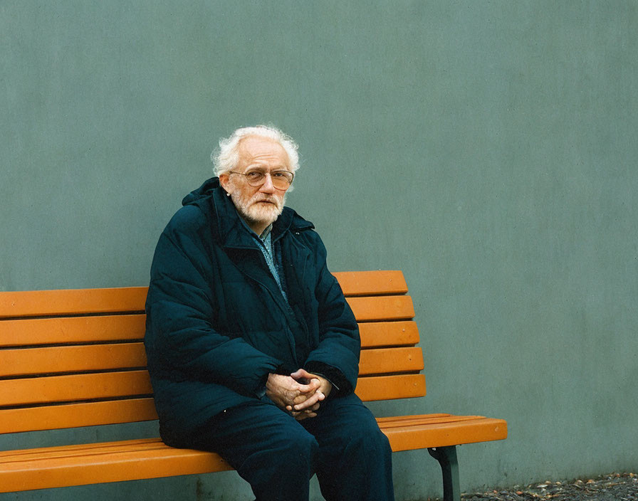 Elderly man with white hair and beard sitting on brown bench in navy coat