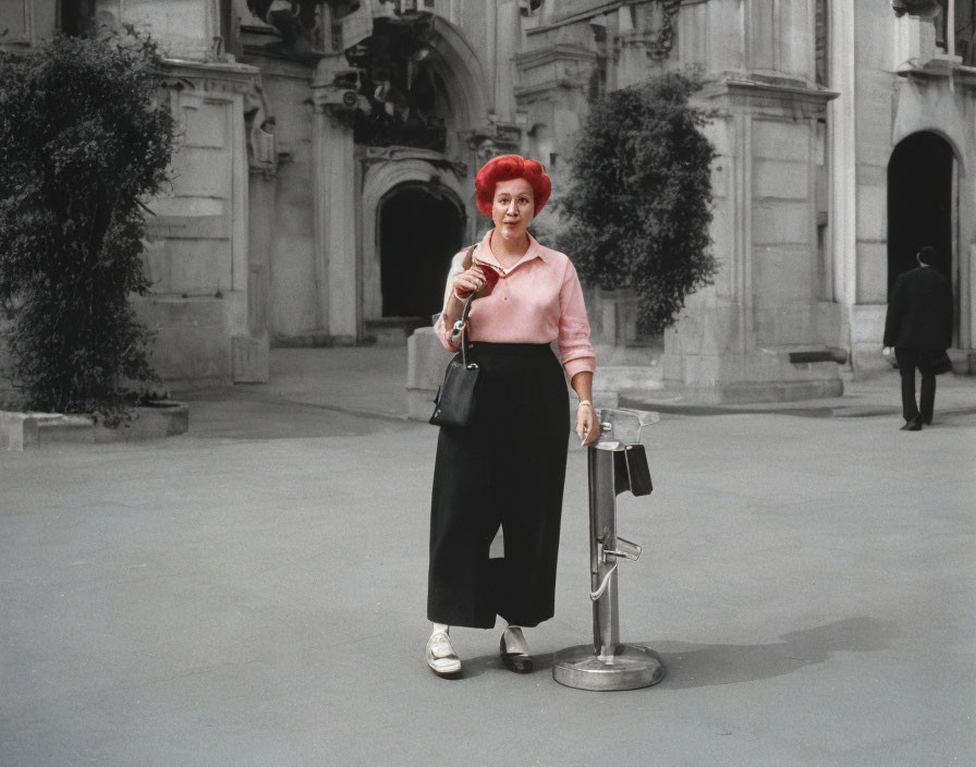 Red-haired woman in pink top and black skirt at courtyard metal barrier with purse and sunglasses