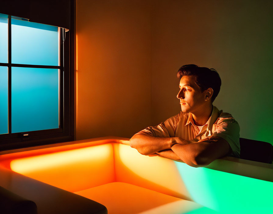 Pensive person in warmly lit room gazes at blue sunset through window