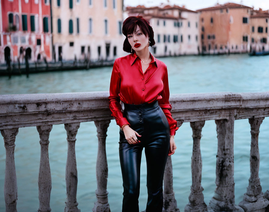 Fashionable woman in red blouse and black pants by canal and colorful buildings