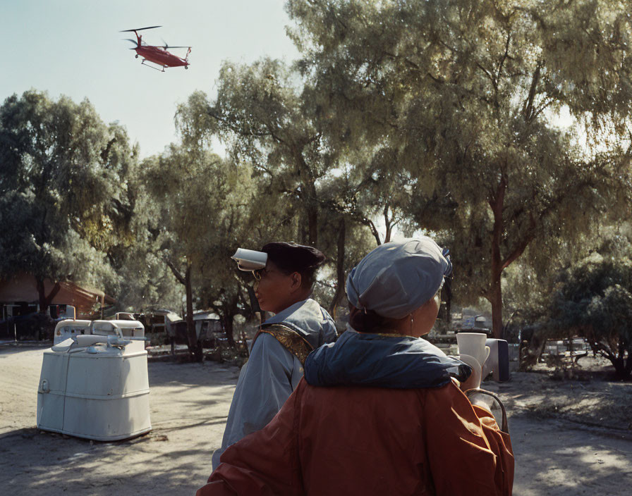 Two Uniformed People Outdoors Watching Helicopter Fly Over Trees