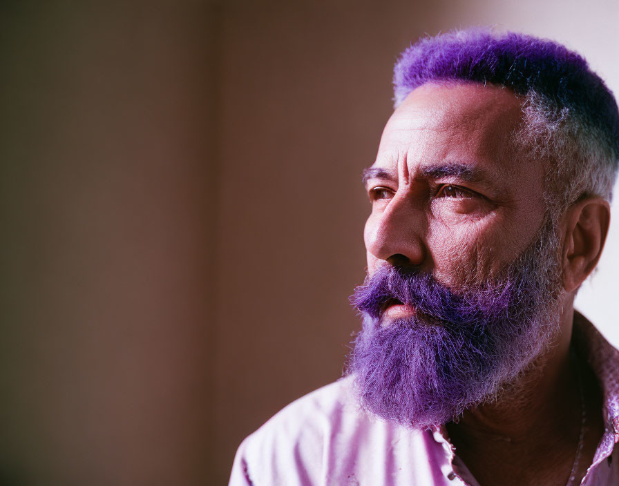 Purple-dyed bearded man looking sideways on blurred background