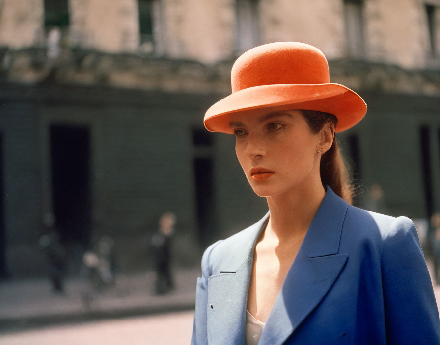 Striking makeup woman in orange hat and blue blazer on city street