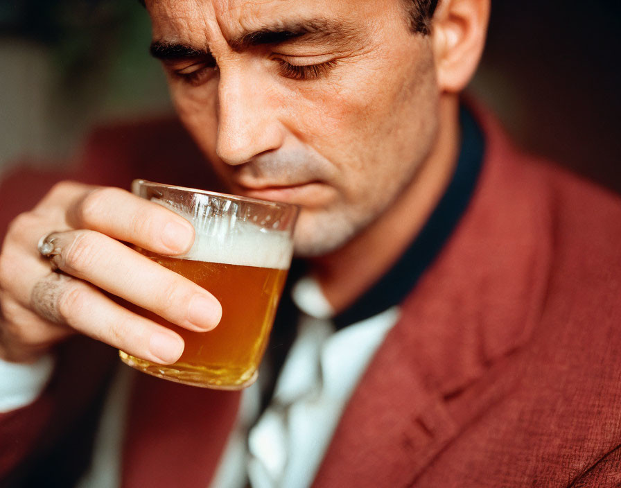 Man in Red Blazer Sipping Beer with Downcast Gaze