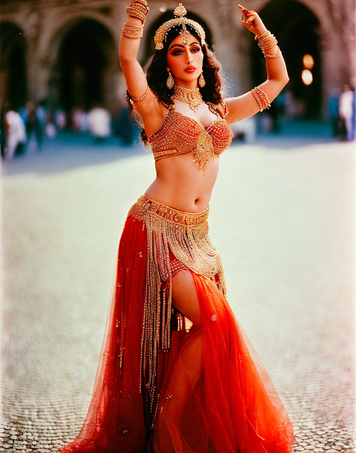 Traditional Indian dancer in red and gold attire poses at historic building