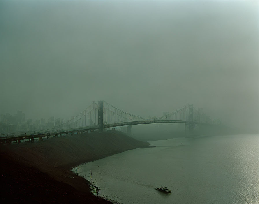 Bridge over water with foggy sky, city silhouette, and boat