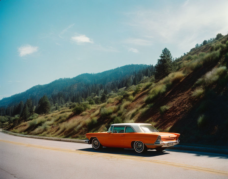 Vintage Orange Car Parked by Forested Hill Under Clear Blue Sky