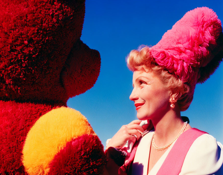 Smiling woman in pink outfit with fur hat and red teddy bear under blue sky