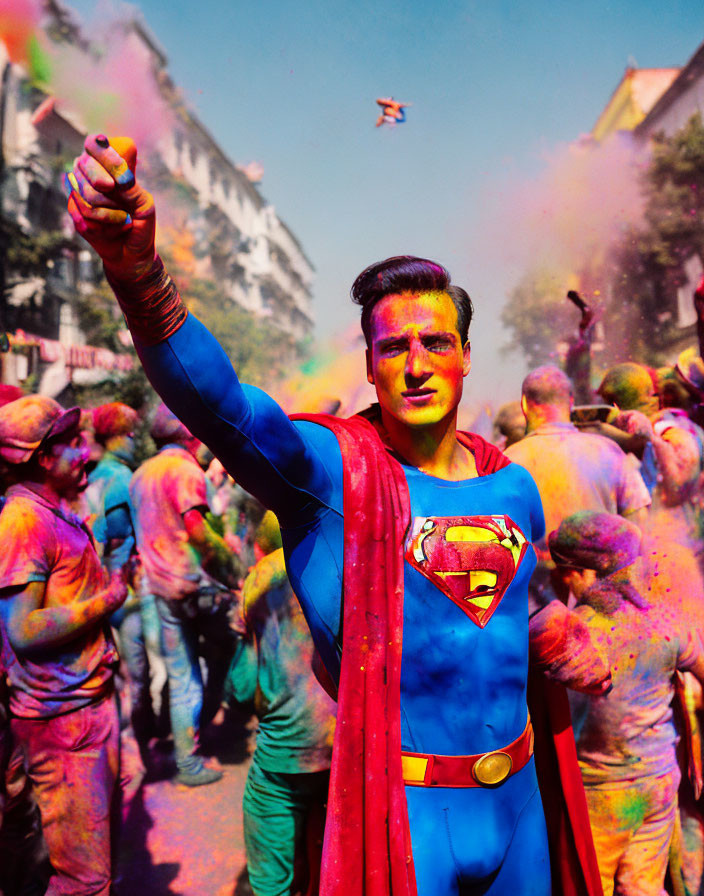 Superman cosplay in vibrant Holi powder cloud with revelers and buildings