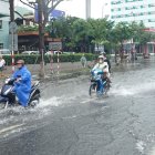 Wet urban street scene: Motorcyclists in heavy rain with splashes, people in rainco