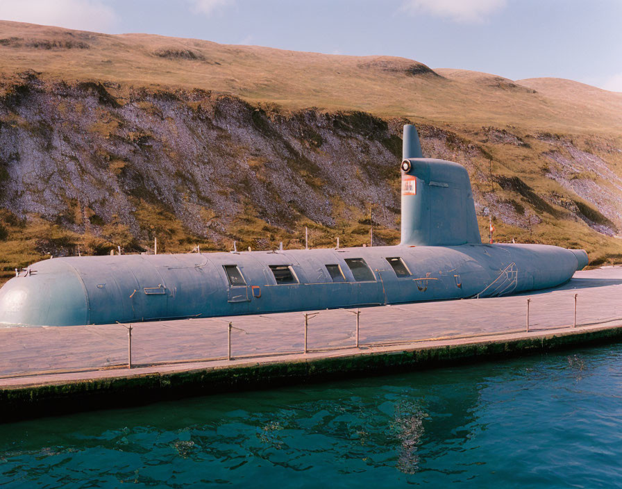 Submarine docked at pier with grassy hill and blue sky