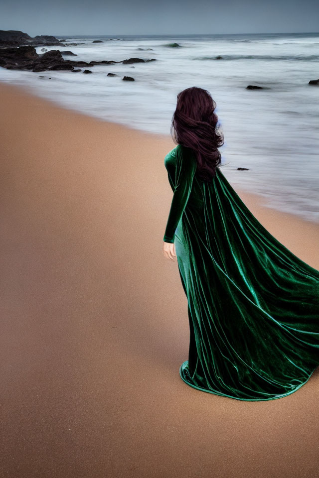 Dark-Haired Person in Green Dress on Sandy Beach with Blurred Waves