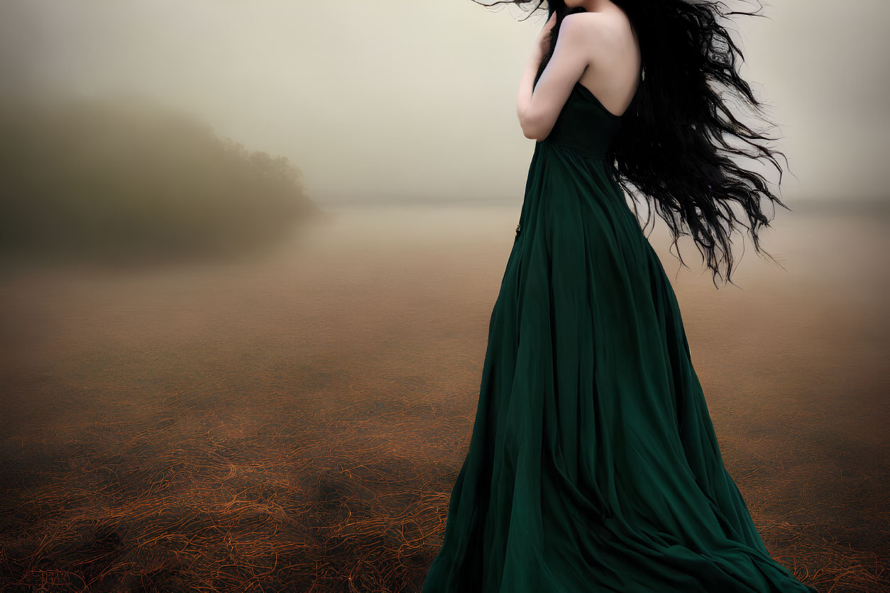 Woman in flowing green dress by foggy water with wind-blown black hair