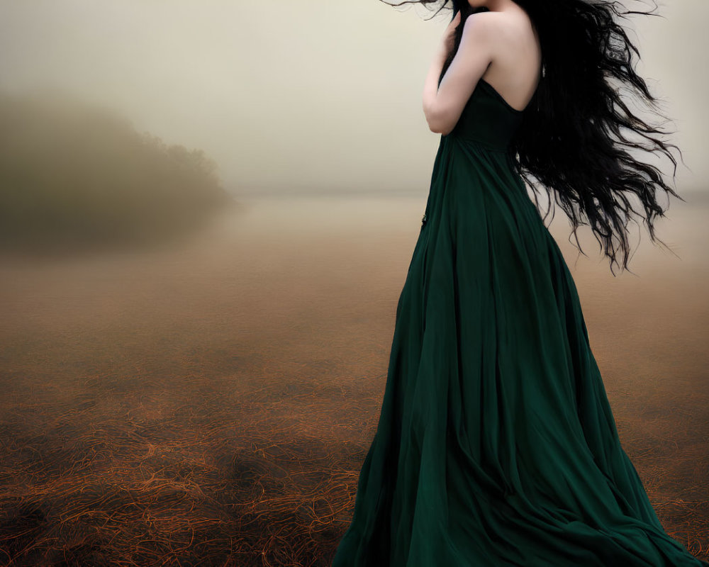 Woman in flowing green dress by foggy water with wind-blown black hair