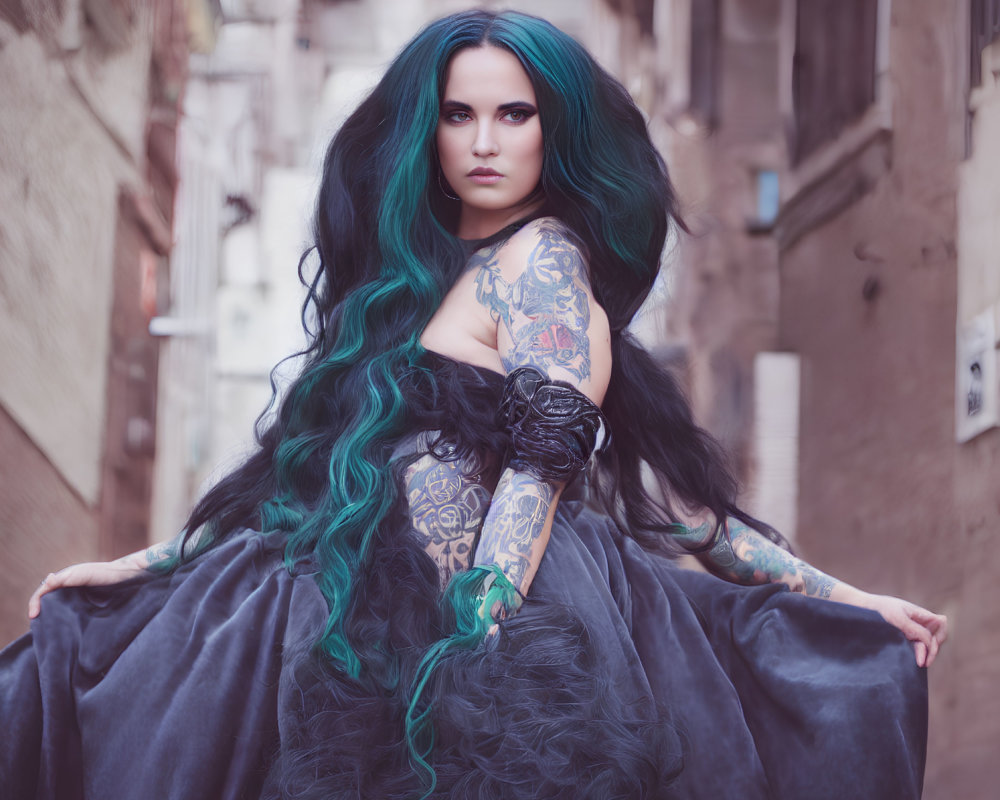 Teal-haired woman with sleeve tattoos in dark dress in alleyway