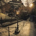 Snow-covered night street with lit lamps, bridge, and gothic building in snowfall.