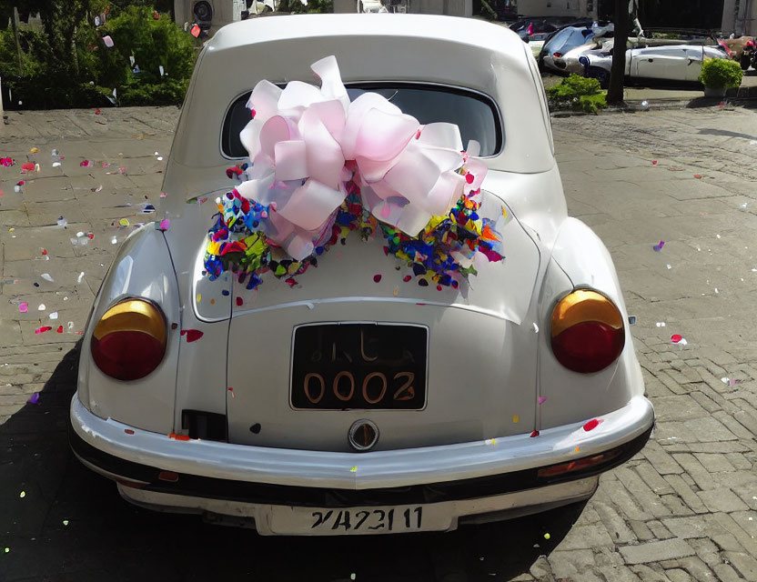 Vintage car adorned with large pink bow and colorful confetti