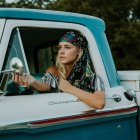 Colorful painting of woman in blue dress driving classic car with vibrant, impressionistic background