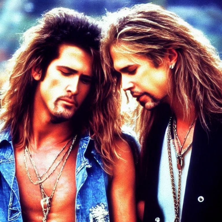 Two individuals with long, styled hair and denim outfits in a classic rock appearance.