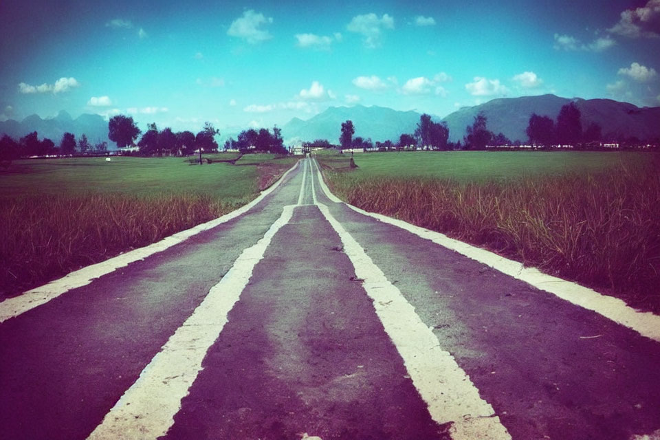 Straight Road Through Green Fields to Distant Mountains