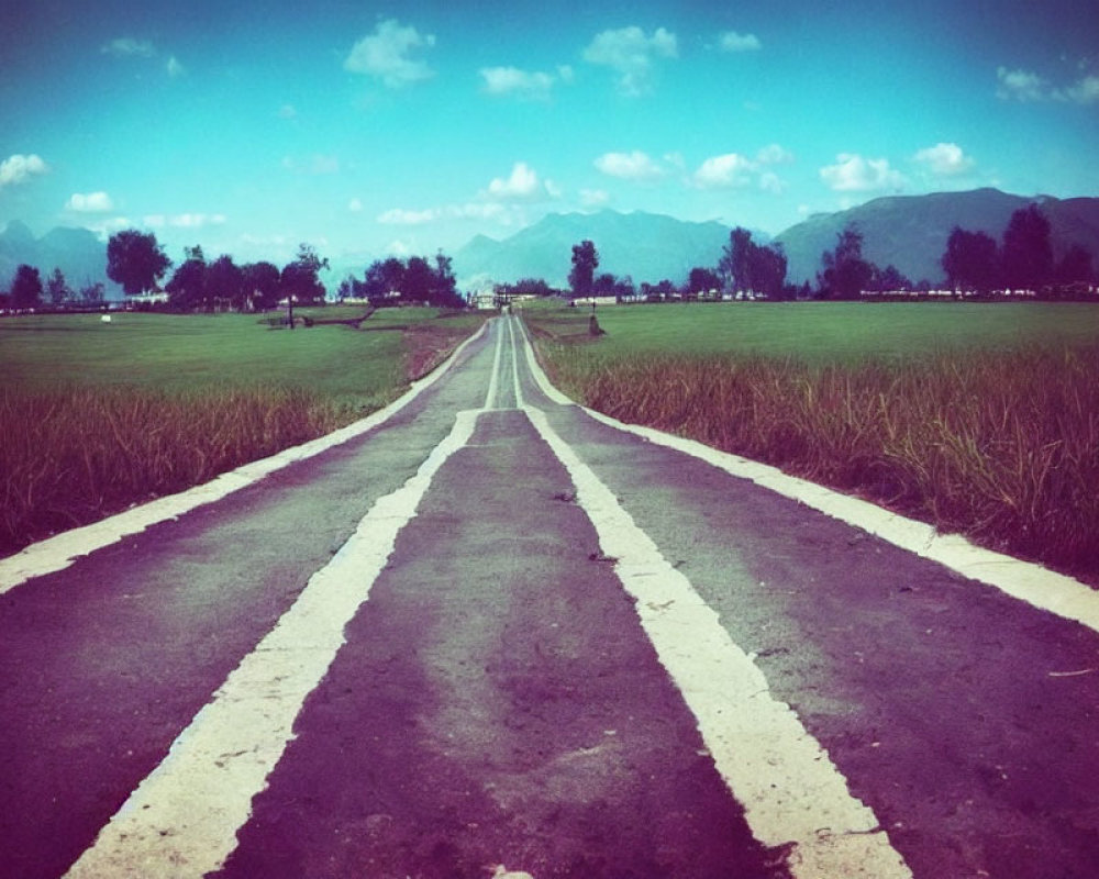 Straight Road Through Green Fields to Distant Mountains