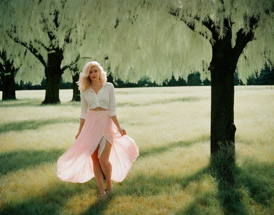 Woman in pink skirt under willow-like trees in sunlight