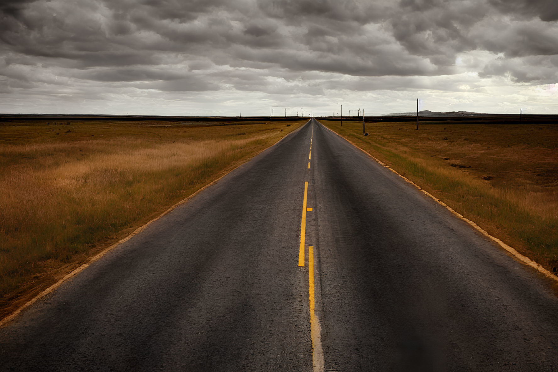 Desolate straight road under dramatic cloudy sky and flat grasslands