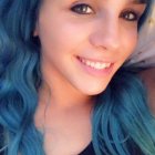 Blue-haired woman with striking blue eyes in soft smile close-up portrait.