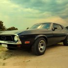 Vintage Black Muscle Car with Iconic Front Grill on Road under Cloudy Sky