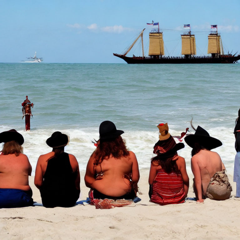 Group of people on sandy beach with tall ship and small boat in distance