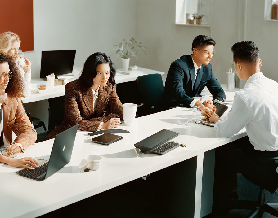 Business professionals in meeting room with laptops and notepads discussing and taking notes