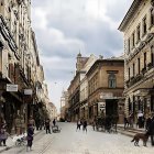 Historic urban street scene with pedestrians and greenery in background skyline