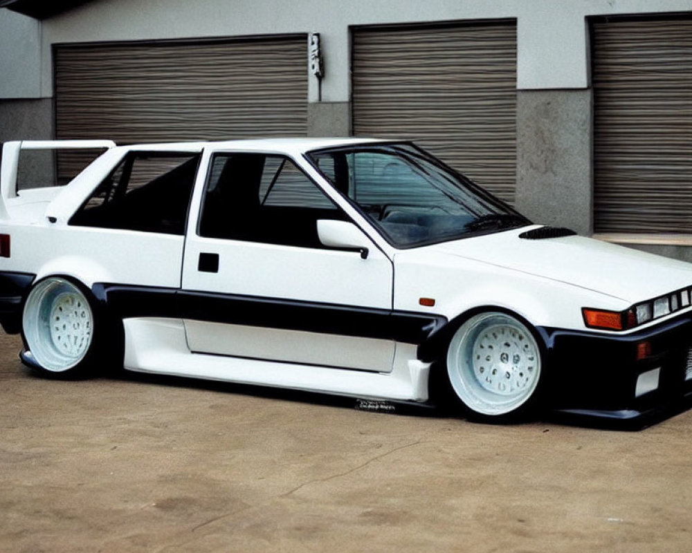 White Vintage Sports Car with Aftermarket Body Kit and Wide Wheels Parked in Front of Industrial Garage Door