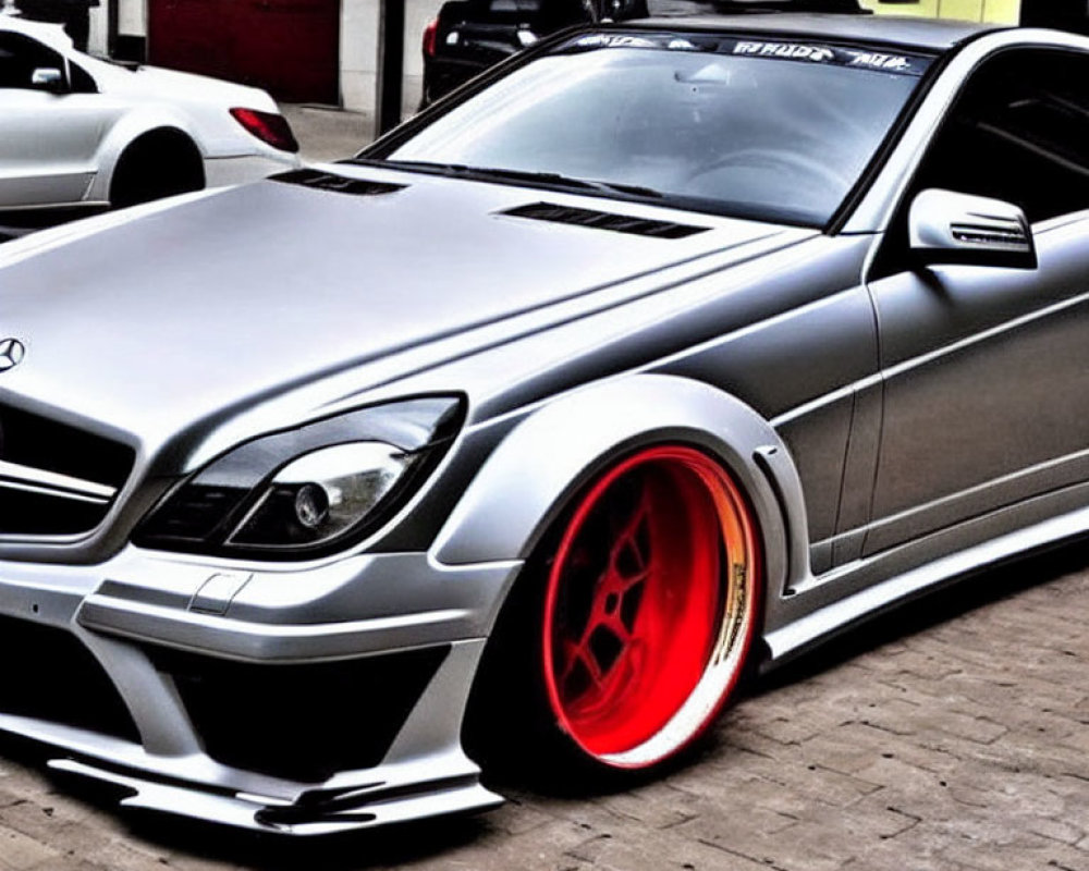 Silver Sports Car with Red-Rimmed Wheels and Wide Body Kit Outside Industrial Building