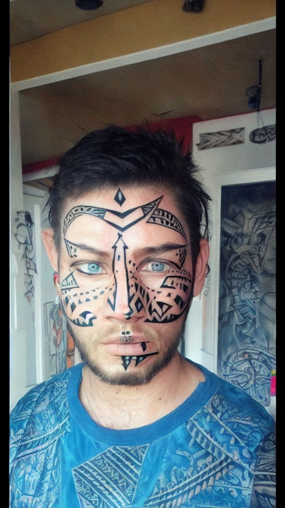 Person with tribal black face paint in front of art wall wearing blue shirt