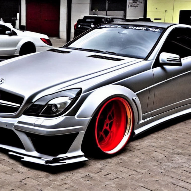 Silver Sports Car with Red-Rimmed Wheels and Wide Body Kit Outside Industrial Building