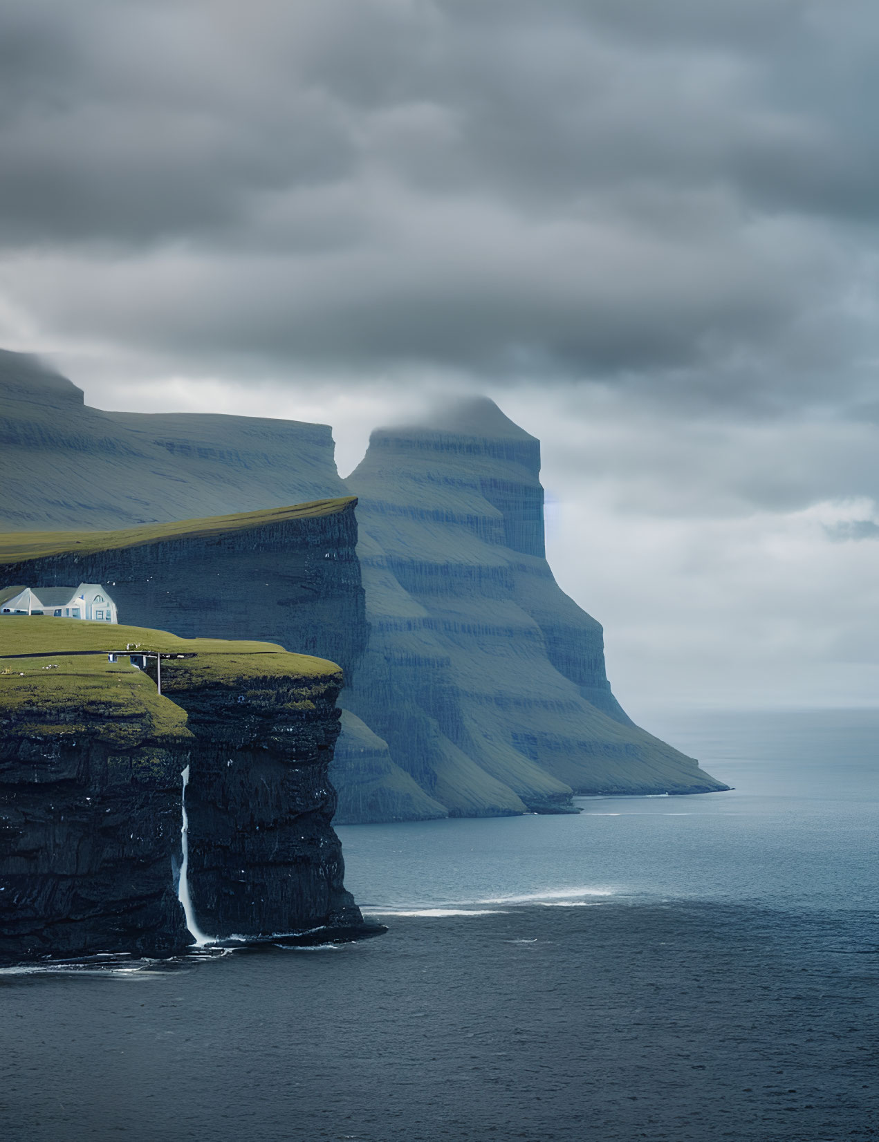 Secluded house on cliff with waterfall, under moody skies