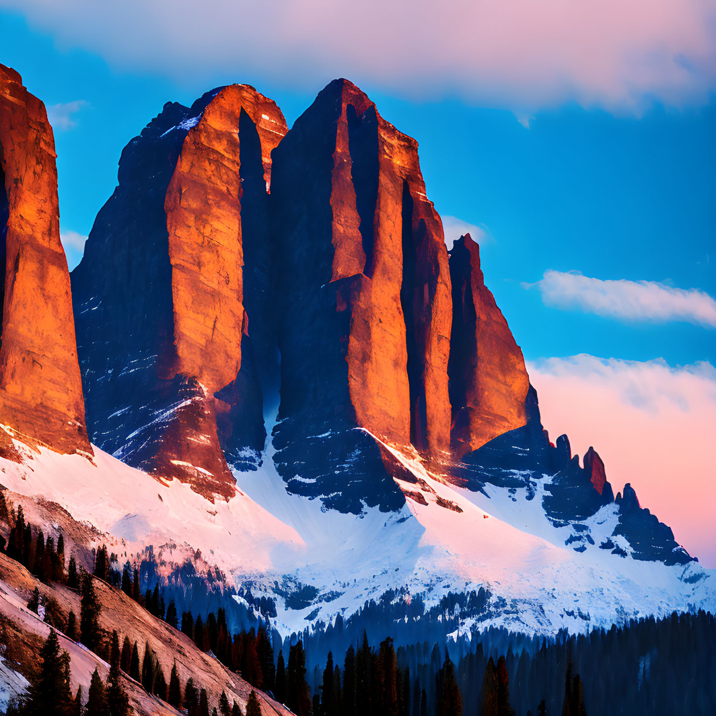 Snowy mountain peaks at sunset over forested landscape under colorful sky