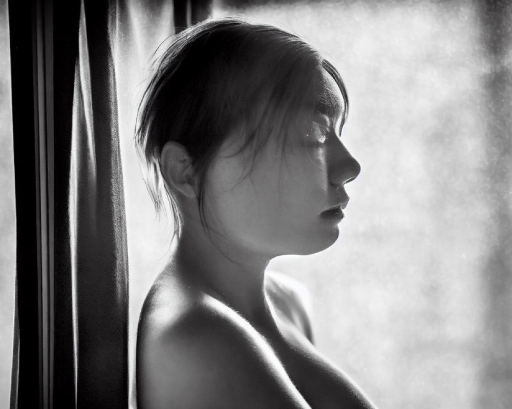 Monochrome profile portrait of woman in contemplative pose with soft window light