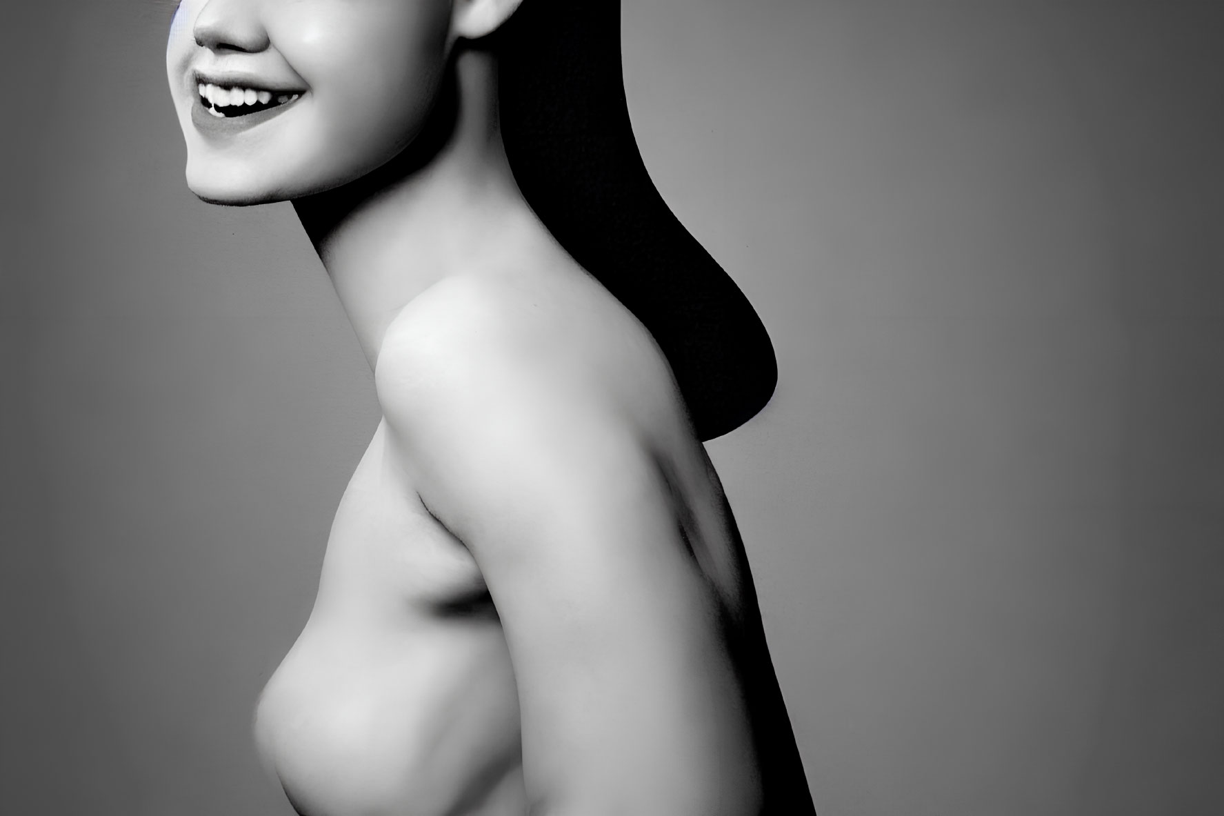 Smiling person's side profile with collarbone and bare shoulders on gray backdrop