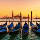 Gondolas on calm water at sunset with distant building and street lamps.