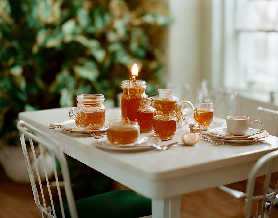 Cozy tea setting with candle, honey jars, cups on white table