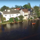 Scenic riverside view: white houses, greenery, boats, reflections, clear sky