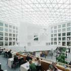 Modern library interior with glass dome ceiling, lush green plants, and curved wooden bookshelves